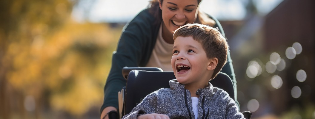 Ein kleiner Junge mit einer Behinderung fährt bei Sonnenuntergang mit seiner Mutter im Rollstuhl. Ein Kind mit Behinderungen