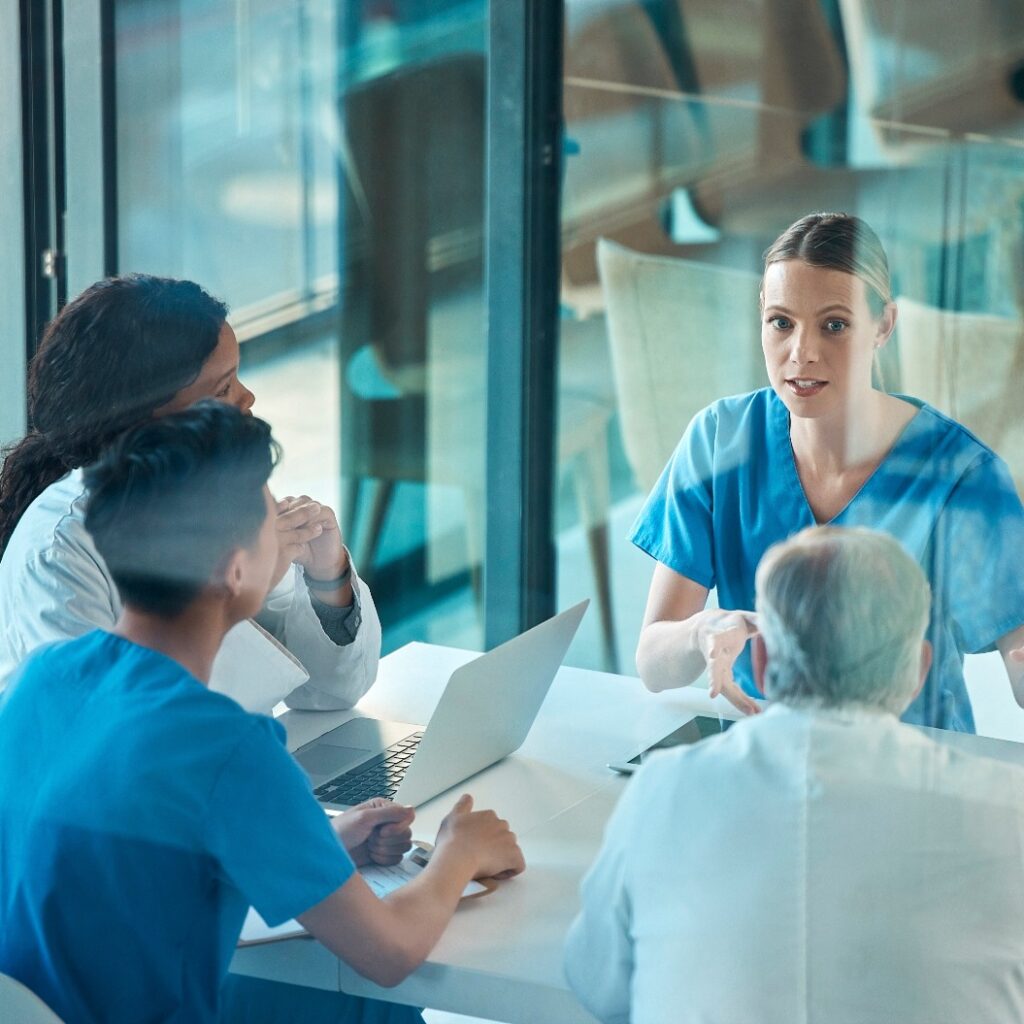 Ein medizinisches Team, Ärzte und eine Besprechung am Tisch mit einem Laptop zur Diskussion, Planung oder Recherche. Eine Gruppe von Männern und Frauen aus dem Gesundheitswesen, die in einem Krankenhaus über Kommunikationsstrategien, Viren oder Operationen sprechen
