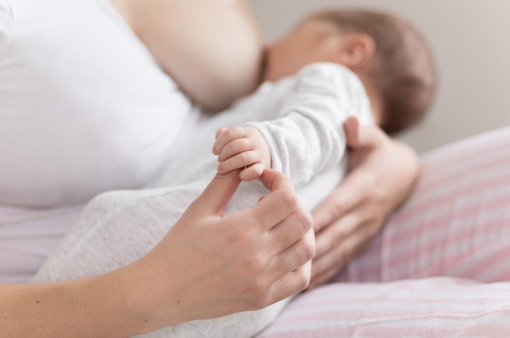 Eine junge Mutter stillt ihren neugeborenen Sohn, während sie ihn zu Hause im Schlafzimmer im Arm hält.