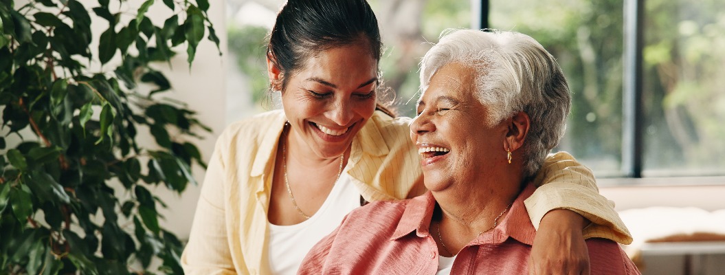 Lachen: Eine ältere Mutter und eine Frau zu Hause mit einem Lächeln, Liebe oder einer Umarmung im Wohnzimmer. Lustig: Eine ältere Mutter und ihre erwachsene Tochter mit einer glücklichen Familie, Verbundenheit und einer Umarmung mit der Mutter am Muttertag