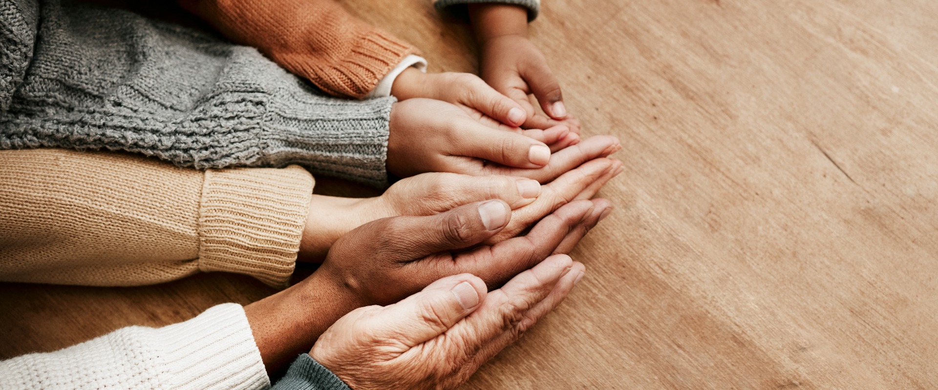 Menschen, die sich an den Händen halten, und Generationen, die sich gegenseitig unterstützen – dargestellt auf einem Modell, das Einheit, Mitgefühl oder Vertrauen symbolisiert, auf einem Holztisch. Eine Gruppe, die sich an den Händen hält, um Unterstützung, Zusammenarbeit, Liebe oder Gemeinschaft im Sinne von Teamarbeit und Solidarität zu verdeutlichen